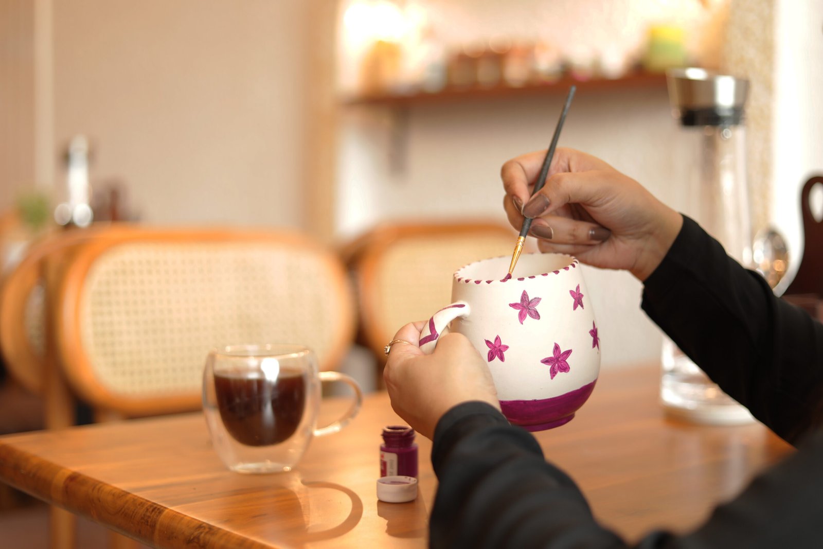A hand painting a colourful ceramic pot with a fine brush