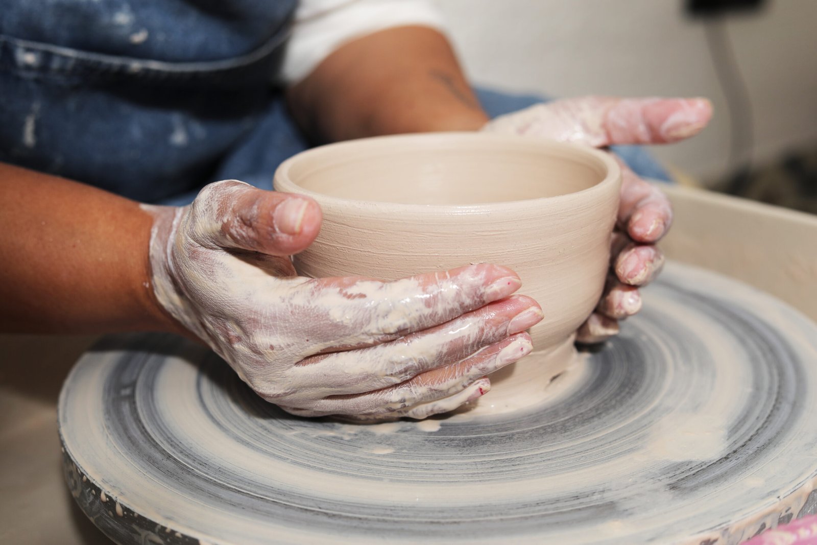 Hands shaping a clay pot on a spinning potter's wheel